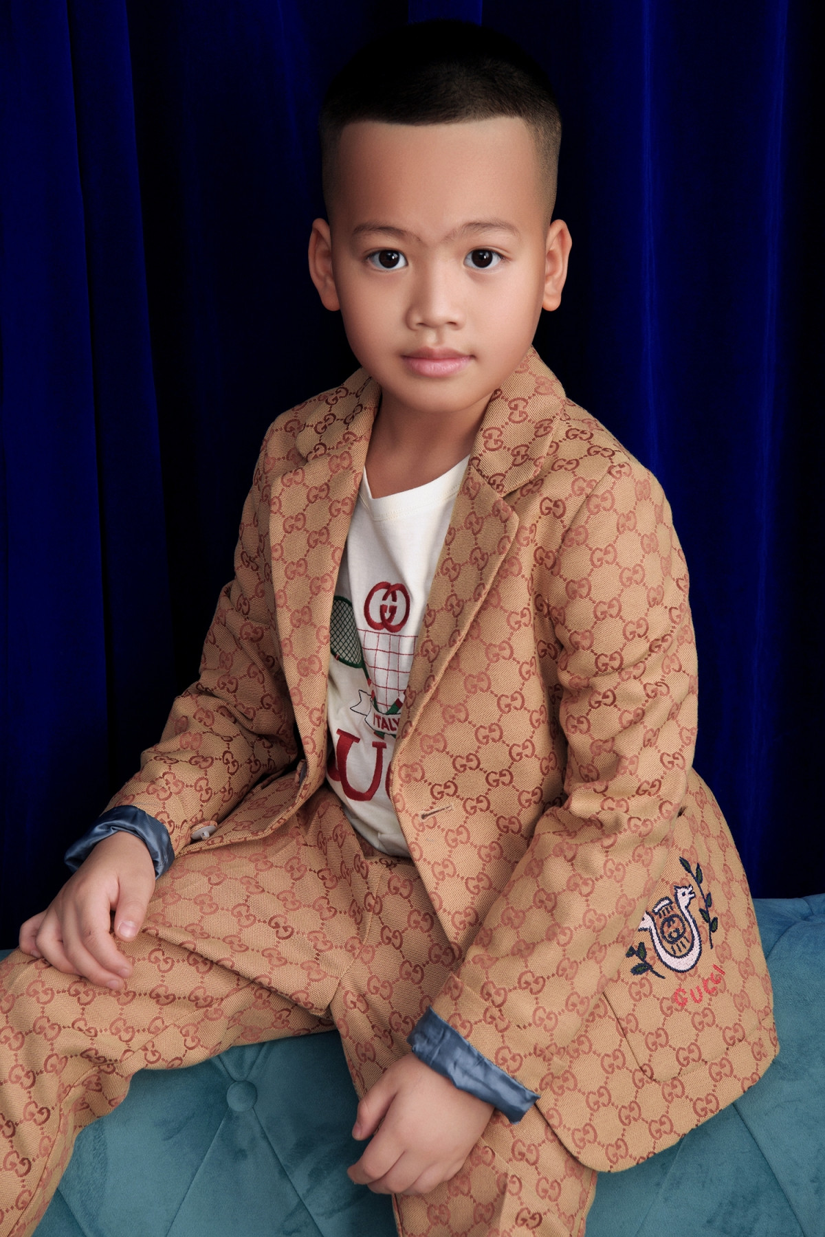 Tít (Đỗ Phạm Gia An) diện vest màu nâu nhạt phối cùng áo thun với hoạ tiết đặc trưng của thương hiệu Gucci. NTK tiết lộ con trai có thiên hướng trở thành người làm việc văn phòng, kinh doanh. 