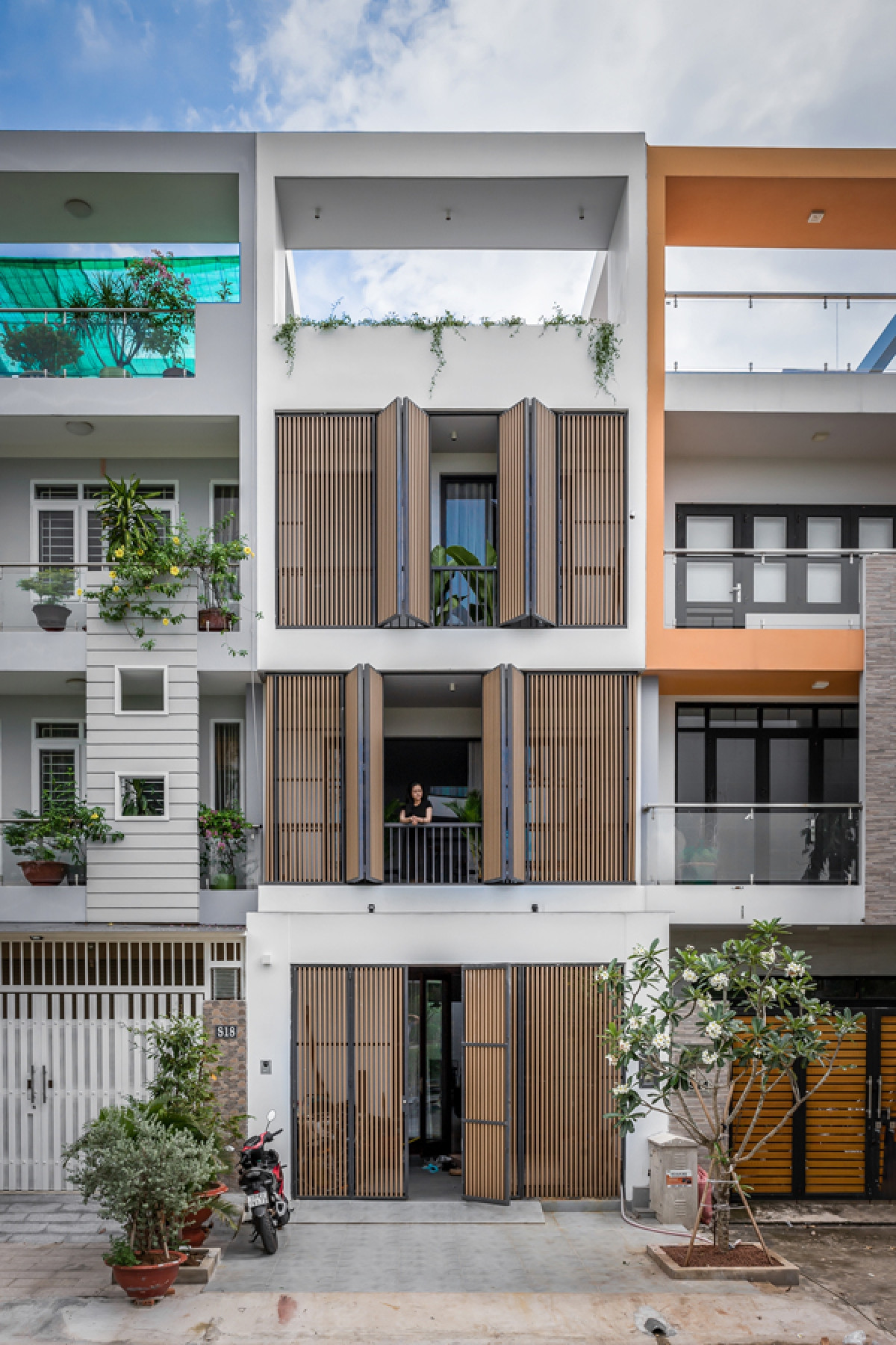 Ngôi nhà có dạng nhà phố nằm trong một khu dân cư mới ở huyện Nhà Bè, TP Hồ Chí Minh. Theo quy hoạch, các lô nhà phải xây đúng quy định về quy mô, chiều cao các tầng. Dù vậy, công trình vẫn có nét riêng nhờ hệ lam phủ mặt tiền, có tác dụng chắn nắng và tạo sự kín đáo nhất định.