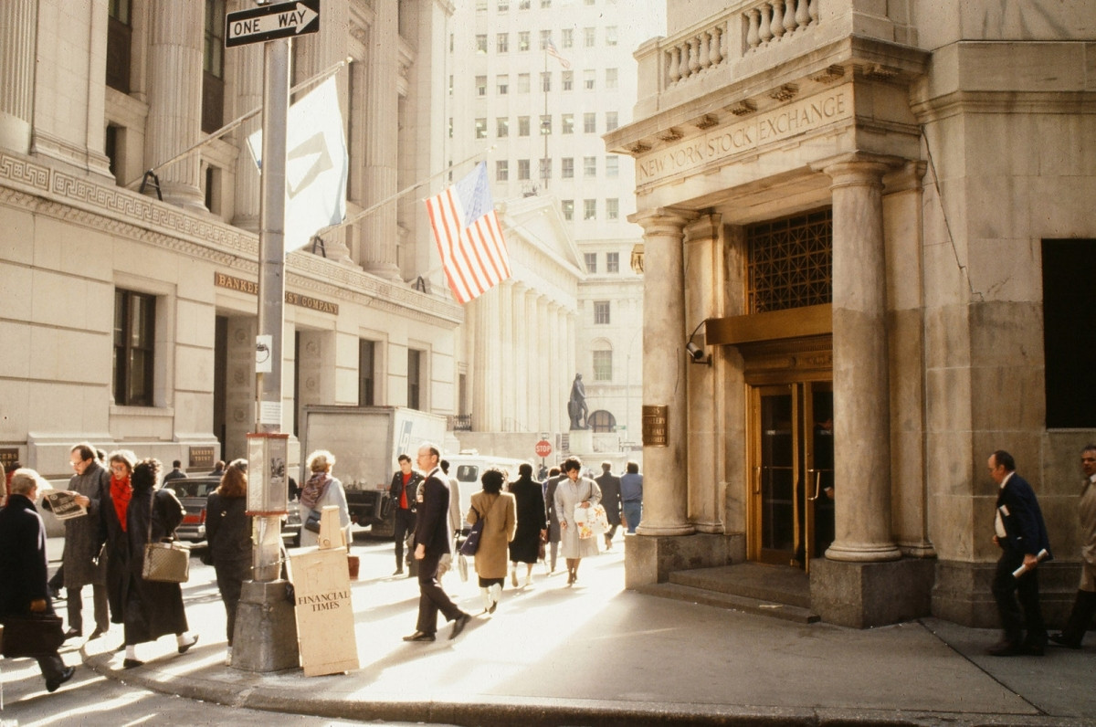 Người đi bộ đi qua lối vào Sở giao dịch chứng khoán New York tại Phố Wall. Những năm 80 là một thập kỷ được đánh dấu bởi sự giàu có, đặc biệt là ở Thành phố New York, một xu hướng tồn tại cho đến khi thị trường chứng khoán sụp đổ năm 1987.
