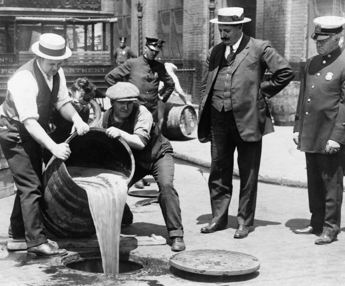 Năm 1921. Phó Ủy viên Cảnh sát John A. Leach (phải) chứng kiến ​​2 người đàn ông đổ rượu xuống ống cống, sau một cuộc truy quét thực hiện lệnh cấm sản xuất và bán rượu. Quốc hội Mỹ đã thông qua Tu chính án thứ 18 vào năm 1920, cấm sản xuất và bán rượu, mở ra thời kỳ 13 năm cấm rượu. Điều này kết thúc với việc thông qua Tu chính án thứ 21 vào năm 1933, bãi bỏ tu chính án thứ 18.