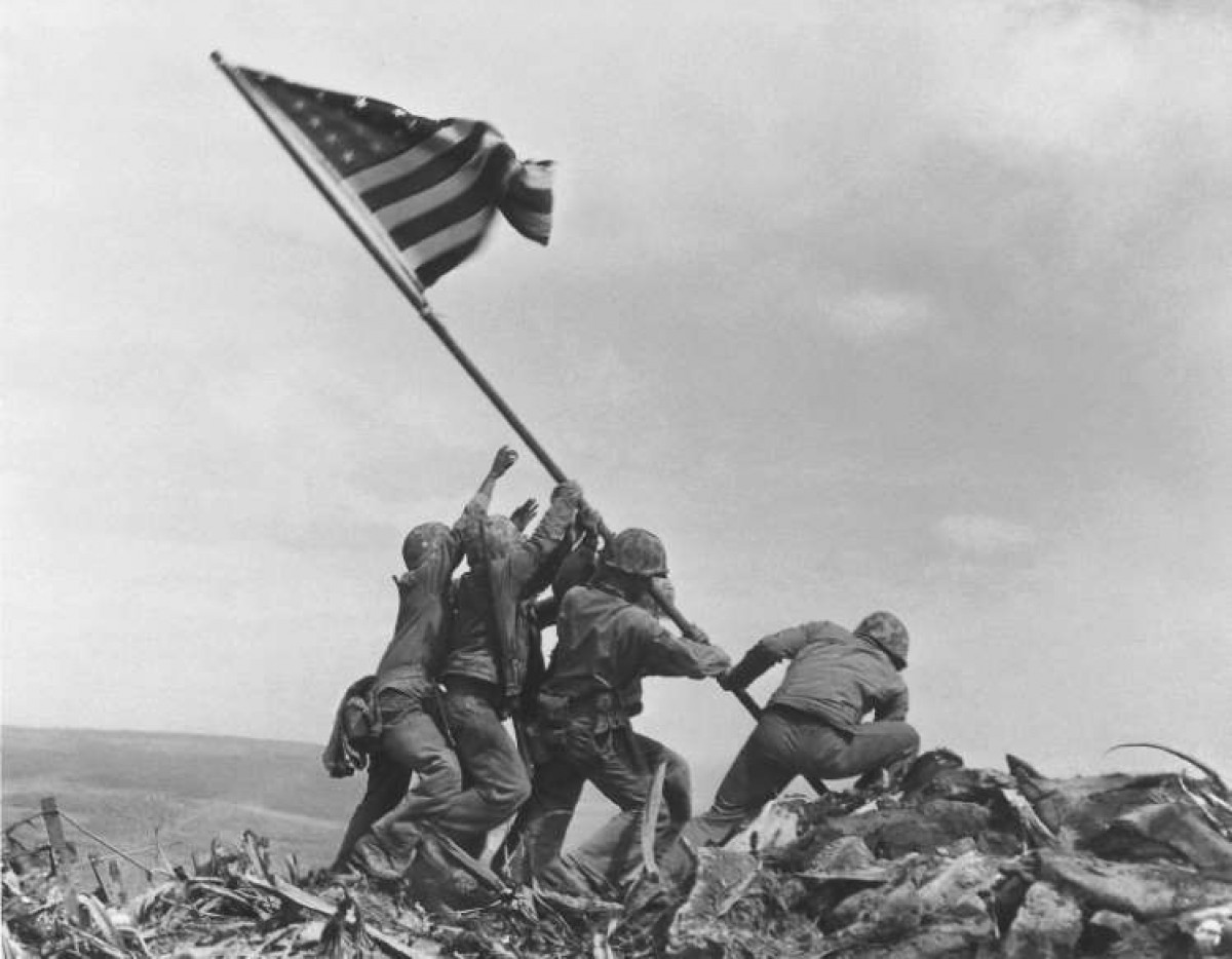 Trong bức ảnh, Thủy quân lục chiến Mỹ thuộc Trung đoàn 28, Sư đoàn 5, giương cao lá cờ Mỹ tại núi Suribachi, Iwo Jima, Nhật Bản, ngày 23/2/1945. Vào tháng 2 năm 1945, quân đội Mỹ tìm cách giành quyền kiểm soát Iwo Jima, một hòn đảo nhỏ gần Nhật Bản làm căn cứ cho chiến dịch trên không nhằm vào các đảo chính của Nhật Bản. Khi lực lượng Mỹ chiếm được núi Suribachi, những người lính đã giương cao lá cờ Mỹ trên ngọn núi. 