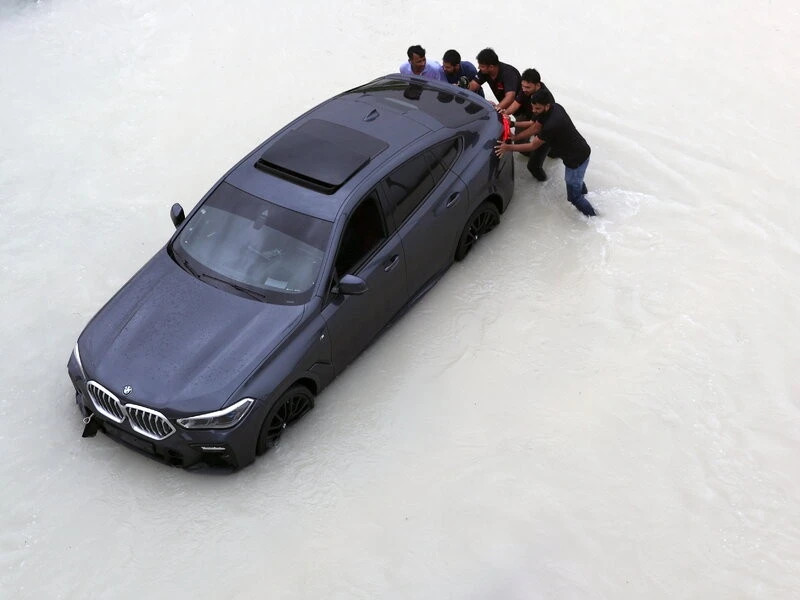 Người dân đẩy chiếc xe BMW trong cơn mưa lớn ở Dubai. (Ảnh: DM)