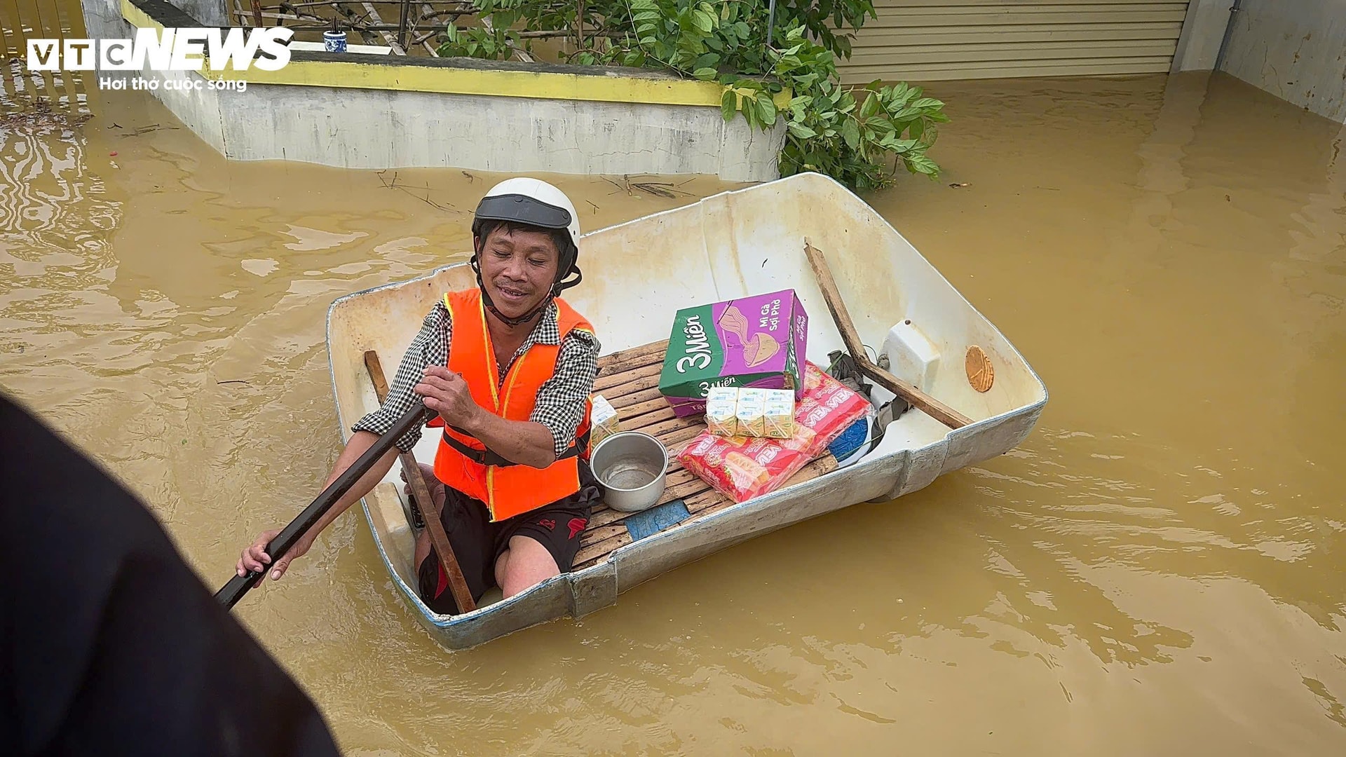 Gia đình ở vùng lụt, nằm xa khu trung tâm, người đàn ông này dùng nửa cái thùng nhựa làm thuyền, chèo ra tuyến đường chính để xin đồ tiếp tế của các đoàn từ thiện. (Ảnh: Nguyễn Vương)