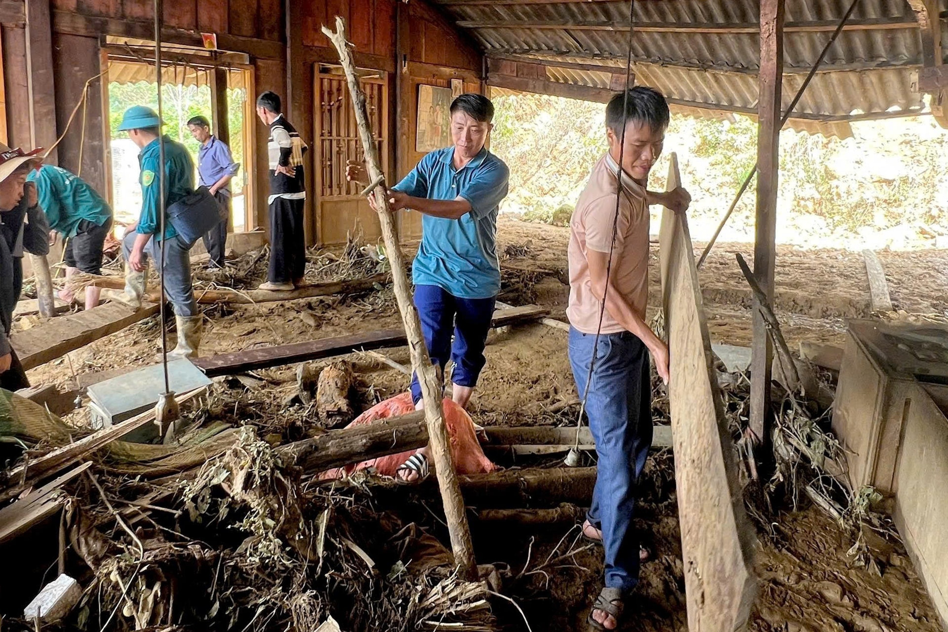 Anh Rình (áo xanh thứ 2 từ phải sang) cùng người dân thôn Giàng Pằng dọn dẹp, dựng lại nhà cho các gia đình bị thiệt hại. (Ảnh: Báo Lào Cai)