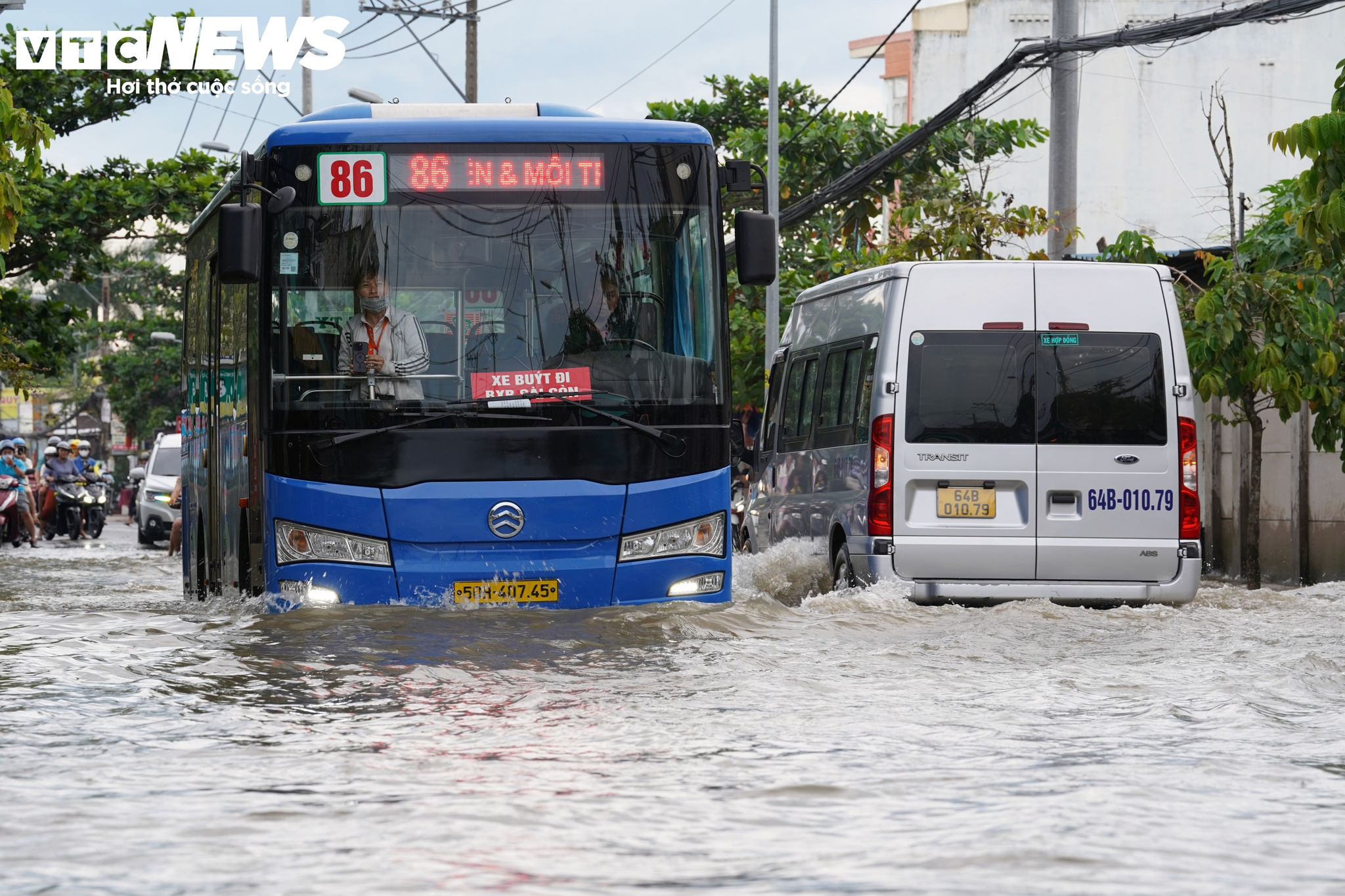 Nước ngập lênh láng trên mặt đường. Mỗi khi xe buýt, ô tô di chuyển nhanh qua khu vực, sóng nước dâng cao, tràn sang hai bên, khiến người đi xe máy chật vật điều khiển phương tiện qua đoạn ngập.